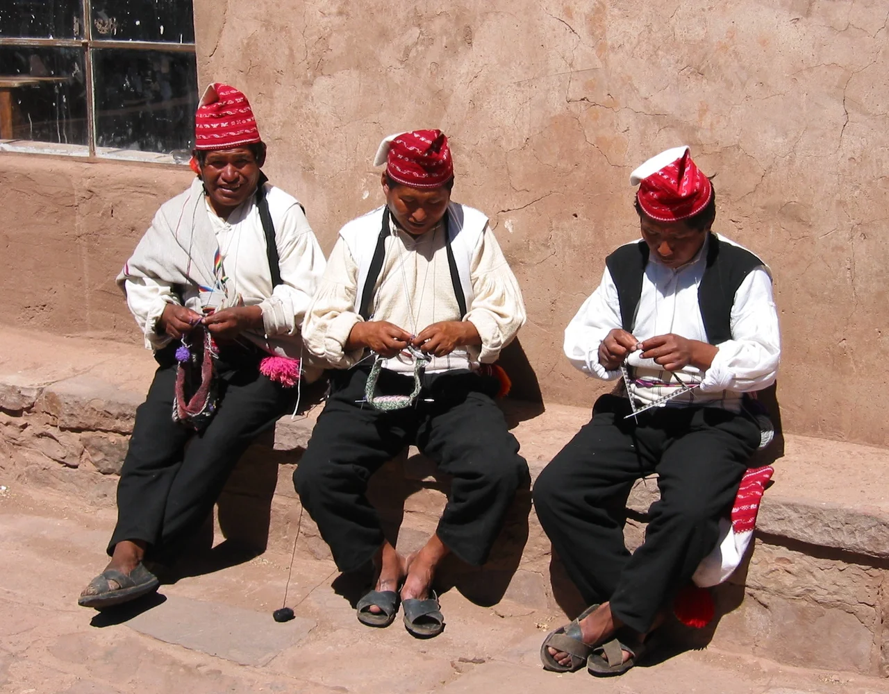 Three men knitting on the Island of Taquile, Lake Titicaca, Peru. The island is known for its textile goods.
