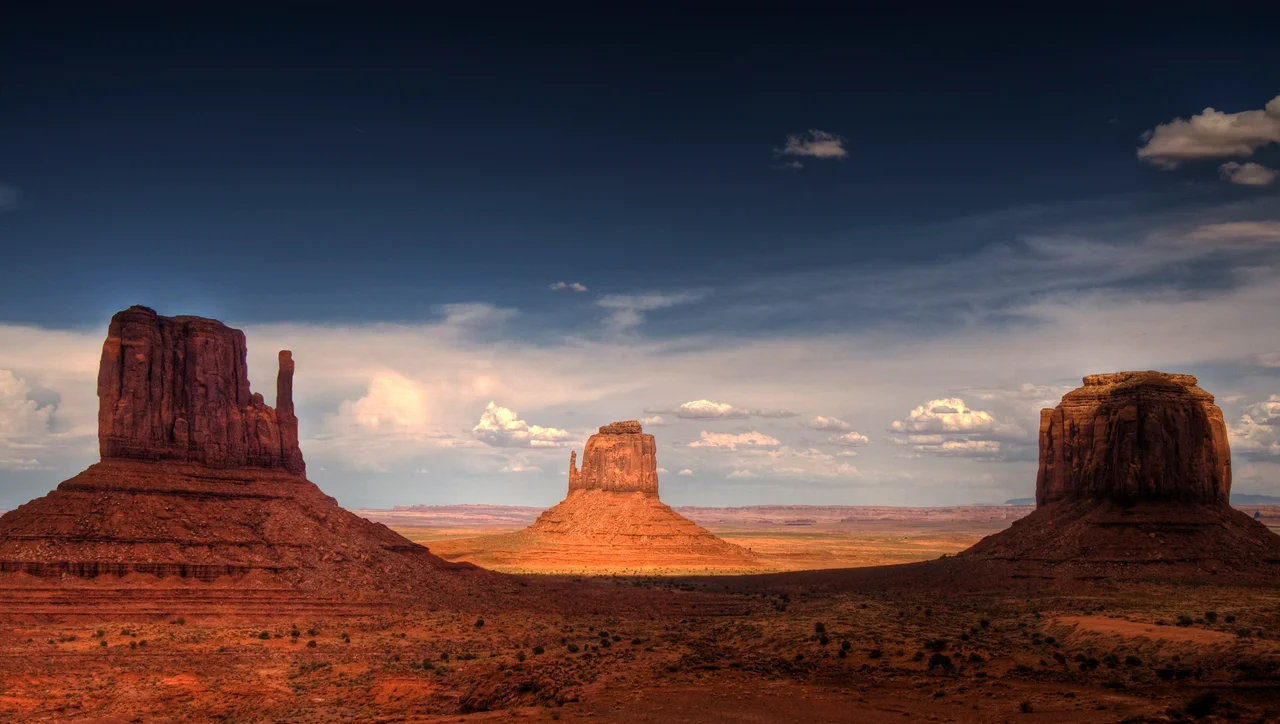 Monument Valley, the buttes are clearly stratified, with three principal layers. The lowest layer is Organ Rock Formation-(skirts, slope-former), the middle De Chelly Sandstone-(vertical cliffs) and the top layer is Moenkopi Formation (shales?, horizontal bedding) capped by Shinarump siltstone-(Shinarump Conglomerate-(locally)). The 3 buttes lie in Arizona, adjacent the Utah border. The en:West and East Mitten Buttes (left & center) are about 1.5 miles (2 km) apart. Merrick Butte is at photo-right.