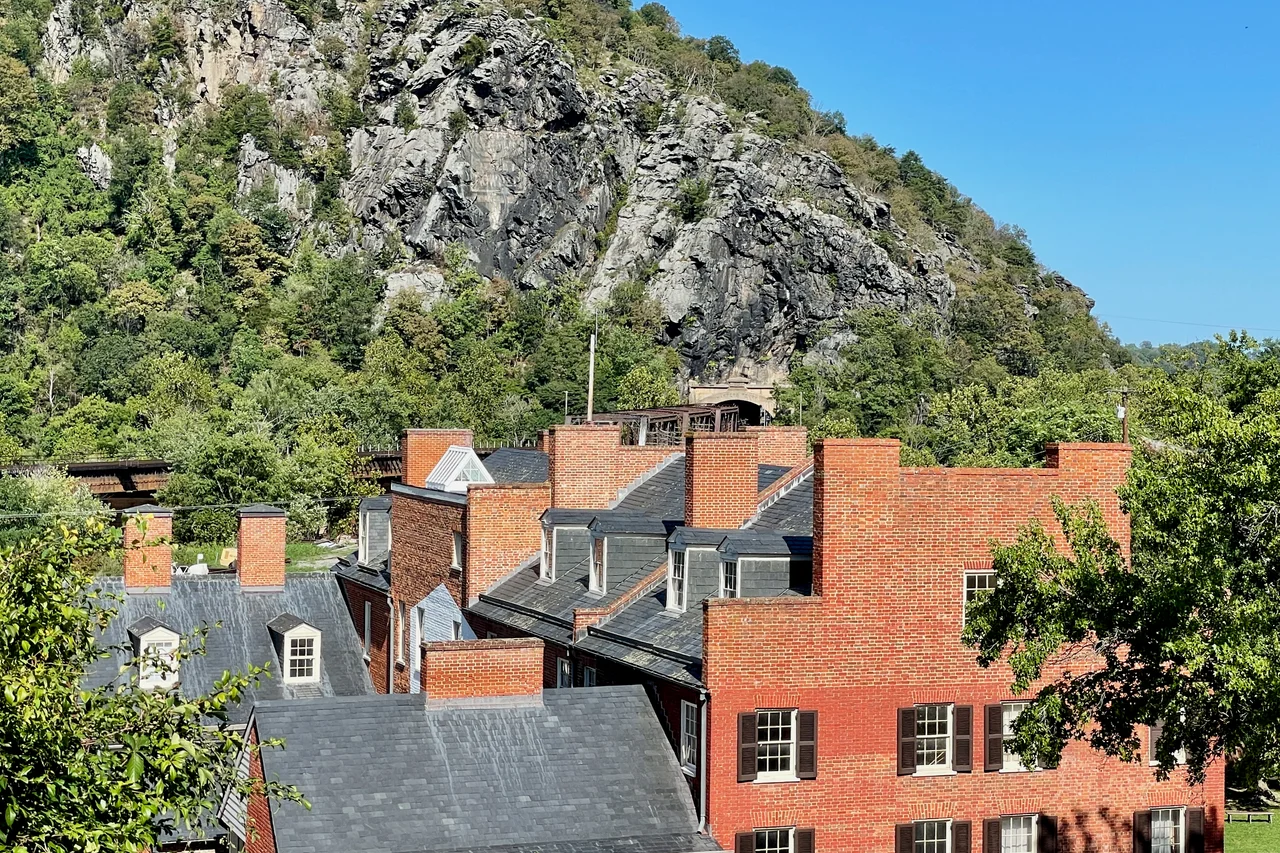 View of brick buildings in the Lower Town section of Harpers Ferry, West Virginia with Maryland Heights and the B & O Railroad Potomac River Crossing in the background. The Mennen's Borated Talcum Toilet Powder advertisement can be seen on the cliff face. Part of the Harpers Ferry National Historical Park.