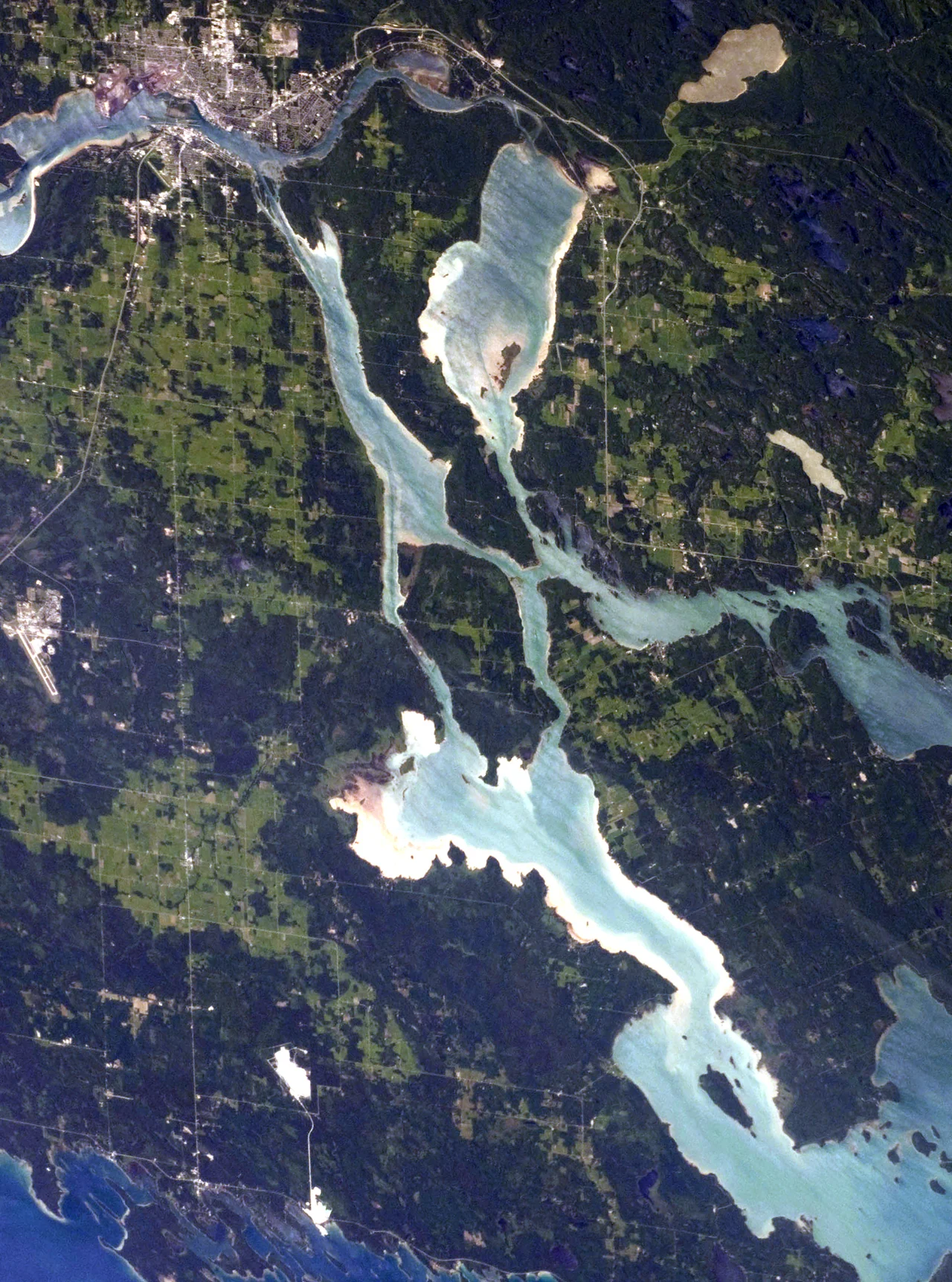 Centred in this astronaut photograph is Neebish Island, Michigan. To the north of it is Sugar Island, Michigan. To the east is St. Joseph Island, Ontario. To the west and south is the eastern corner of Michigan's upper peninsula. The twin cities of Sault Ste Marie, Ontario and Michigan can be seen in the upper right hand corner. These are located across the St. Marys River, which forms part of the international boundary between Canada (Province of Ontario) and the United States (State of Michigan). These urban areas have a distinctive gray to white colour, contrasting with the deep green of forested areas in Ontario and the lighter green of agricultural fields in Michigan. The water surfaces in the lakes and rivers vary from blue to blue-green to silver, likely the result of varying degrees of sediment and sunglint—light reflecting from the water surface back to the International Space Station.