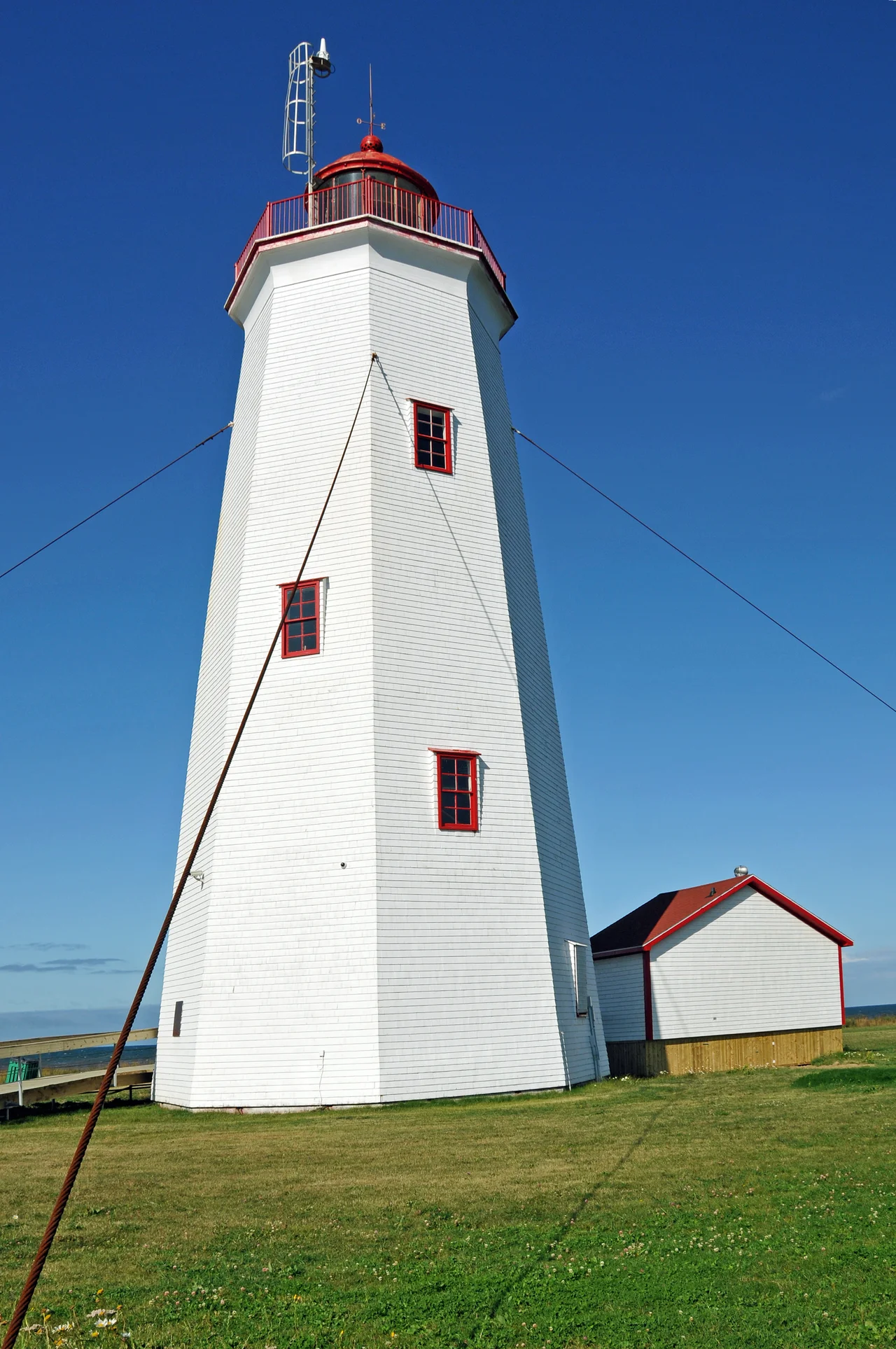 Miscou Island Lighthouse
This lighthouse was built in 1856 at the southern entrance to Chaleur Bay by Quebec Trinity House, which then supervices navigation on the St. Lawrence River and Gulf. Considered a major coastal aid it merited the subsequent installation of a powerful dioptric light and a diaphone fog alarm. The octagonal tower of hand-sawn timbers, shingled on the outside, was originally 74 feet in height and was extended in 1903 to 80 feet. This lighthouse, substantially in its original state, is among the oldest in the Gulf of St. Lawrence region.
The lantern at Miscou Island houses a functioning third-order Fresnel lens, the only Fresnel lens still operating in an authentic lighthouse in New Brunswick. After an environmental cleanup in 2008, the province undertook a large scale project to make this a major tourist destination in the region. A paved parking area (large enough for tour buses), a deck around the lighthouse and washroom facilities in addition to a large grass area are completed.