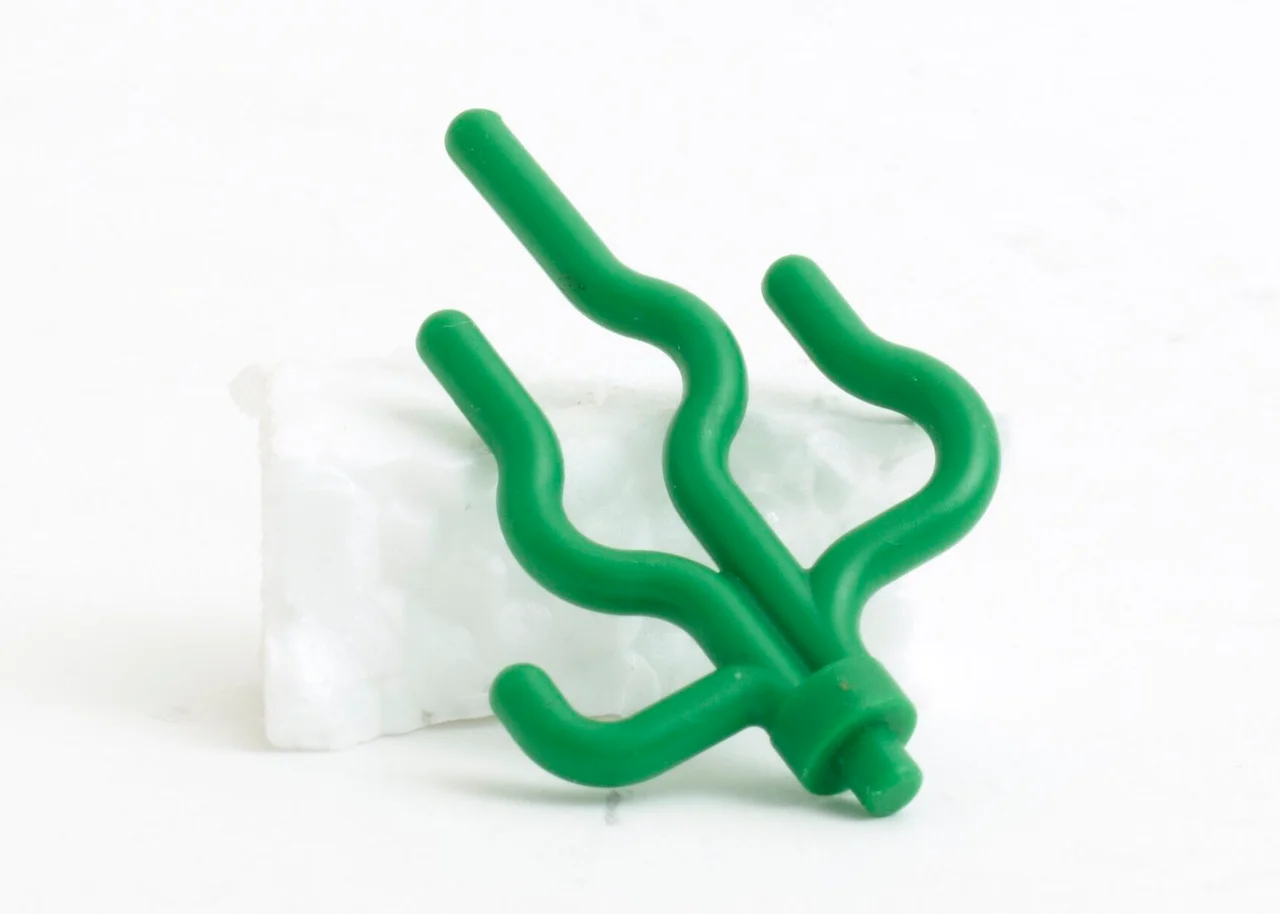 A small green plastic LEGO accessory shaped like a patch of seaweed. This piece was part of the Lego Lost at Sea Project, started by Tracey Williams. On February 13, 1997, approximately five million LEGO pieces were spilled into the sea when a wave capsized a cargo ship carrying a shipment of the toys off the coast of Cornwall, England. In a twist of irony, many of the pieces were sea creature themed. To this day, beachcombers still uncover washed-up plastic pieces from this monumental toy-related environmental disaster.