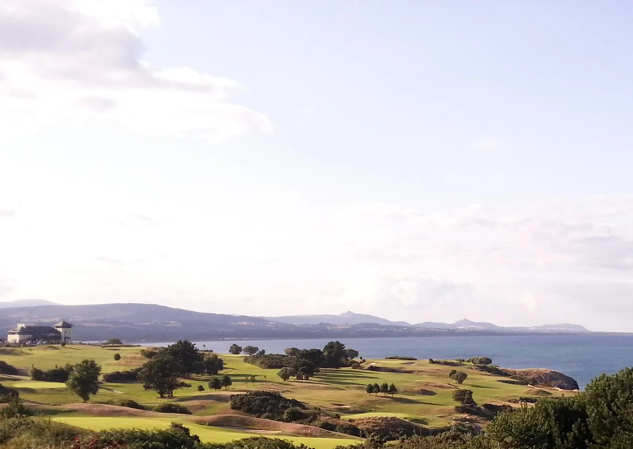 This is a photo showing the geographical context of Wicklow town with its coastline to the south, its bay and the hills and headlands to the north. Wicklow town itself is not in view, hidden below Wicklow golf club house