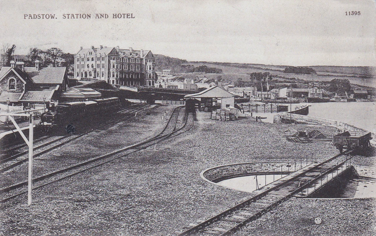 A view of Padstow railway station, Cornwall, England. A train is in the platform, and the station is a terminus. A fish shed is in the centre of the frame, used for transferring fish from vessels in the small dock on the right into railway vans. A turntable for the engines is at the right. The view is to the north west.