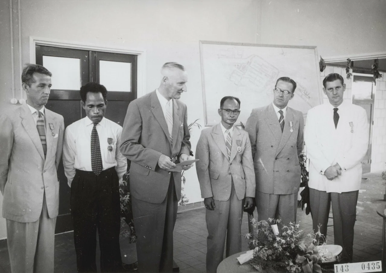 Opening Centraal Ziekenhuis te Hollandia - Nederlands Nieuw Guinea: Uitreiking decoraties. Van links naar rechts: 1. men. Petersen, Opzichter bouw Ziekenhuis (in dienst van het Gouvernement): Koninklijke Onderscheiding, 2. men. Rumainum: Onderscheiding van het Gouvernement, 3. men. Zuiderhoek: Hoofd Dienst van Volksgezondheid houdt toespraak, 4. men. Mandosir: Onderscheiding van het Gouvernement, 5. men. ? : Uitvoerder (in dienst van samenwerkende bouwonderneming): Koninklijke Onderscheiding, 6. men. Gerrit Palsgraaf: Hoofduitvoerder Bouwmij Hollandia BMH: Koninklijke Onderscheiding.