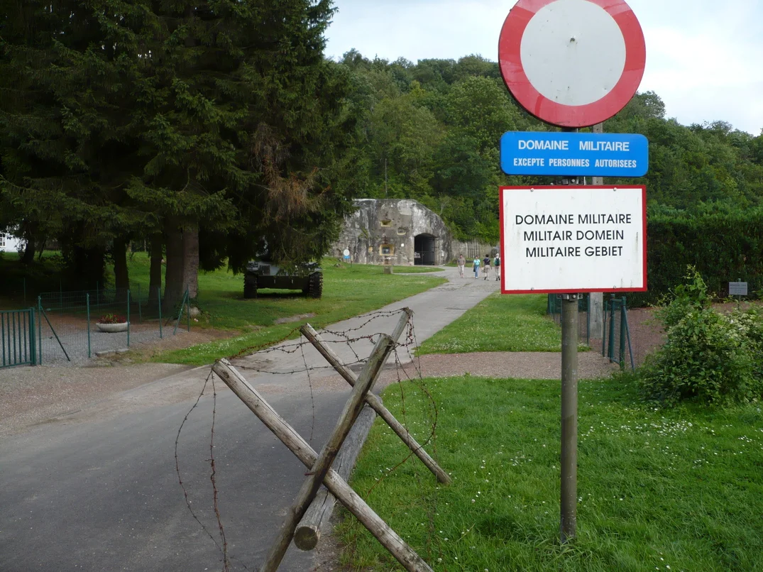 Entrance to Fort Eben-Emael in Belgium, July 2007. DeMinimis applies here. This is Bloc 1, a two level concrete blockhouse, seen from the south (i.e. from the approach road outside the fortress), with three embrasures visible to the left of the entrance. The lowest one mounted a 60mm anti tank gun, the one directly above it a machine gun, and the one offset to the right a searchlight. Garrison was 5 NCOs and 23 soldiers. Contemporary photos show vegetation was much thinner when the fortress was in use.