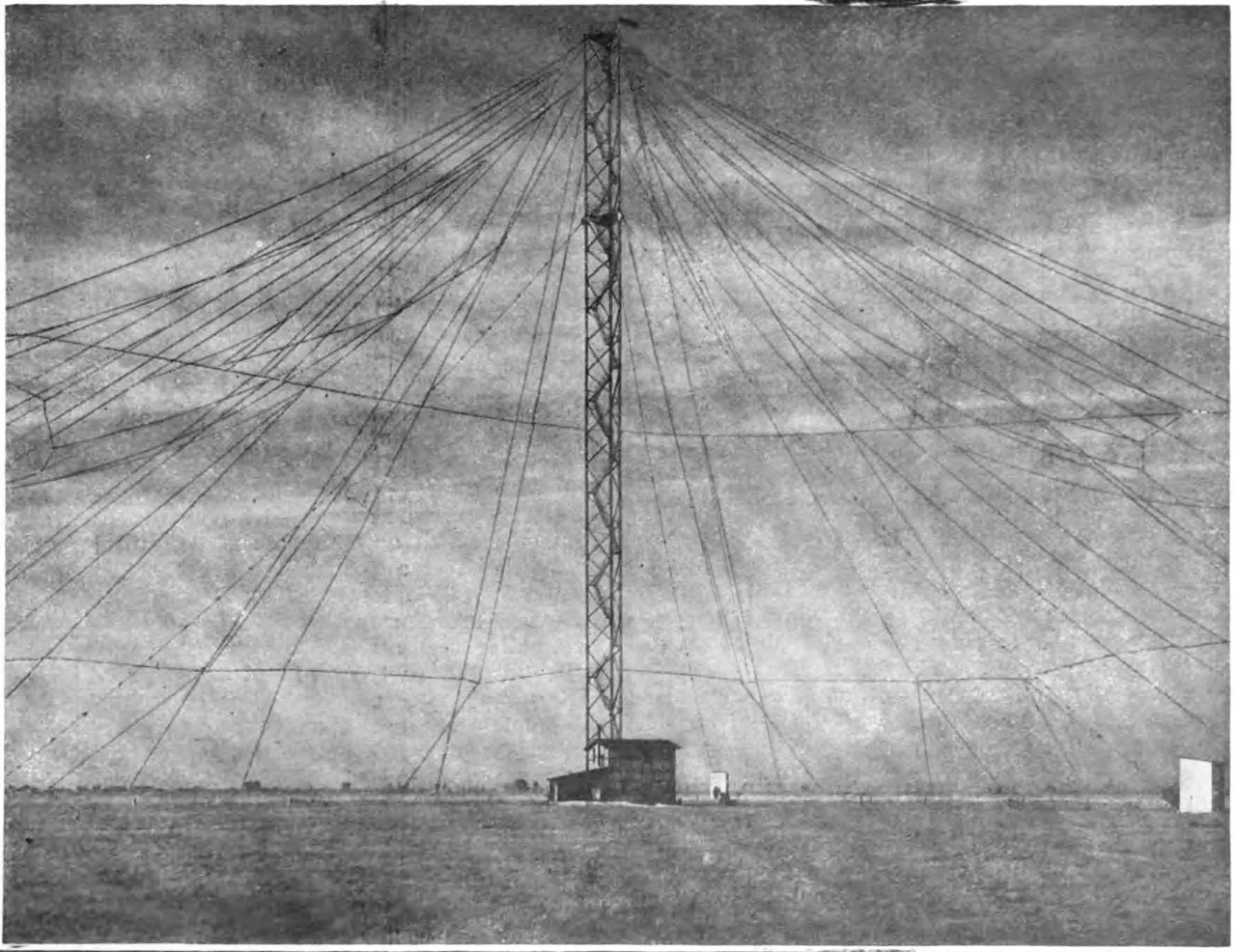 A large umbrella antenna used as the transmitting antenna for the transatlantic wireless telegraphy radio station, Nauen Transmitter Station, built by Gesellshaft fur Drahtlose Telegraphie at Nauen, Germany in 1906, which served as Germany's main communication channel with other nations during World War 1. It consisted of a steel truss tower 100 meters (328 feet) tall, insulated from the ground, attached to the transmitter, with a radial network of cables extending diagonally from the top, anchored to the ground at a distance of 200 m from the tower. The bottom end of the 162 umbrella cables were attached to the three ground anchors with hemp ropes, so the umbrella was insulated from the ground. The surface area of the umbrella was 60,000 square meters (646,000 sq. ft. or about 15 acres). The Nauen spark transmitter had an input power of 35 horsepower (26 kilowatts) and radiated in the very low frequency band. The vertical tower served as an electrically short monopole mast radiator and the radial cables served as a capacitive top load to increase the current in the radiator. The other side of the transmitter was connected to a ground (Earth) system consisting of 108 buried cables radiating from the tower, covering 126,000 square meters or about 31 acres.