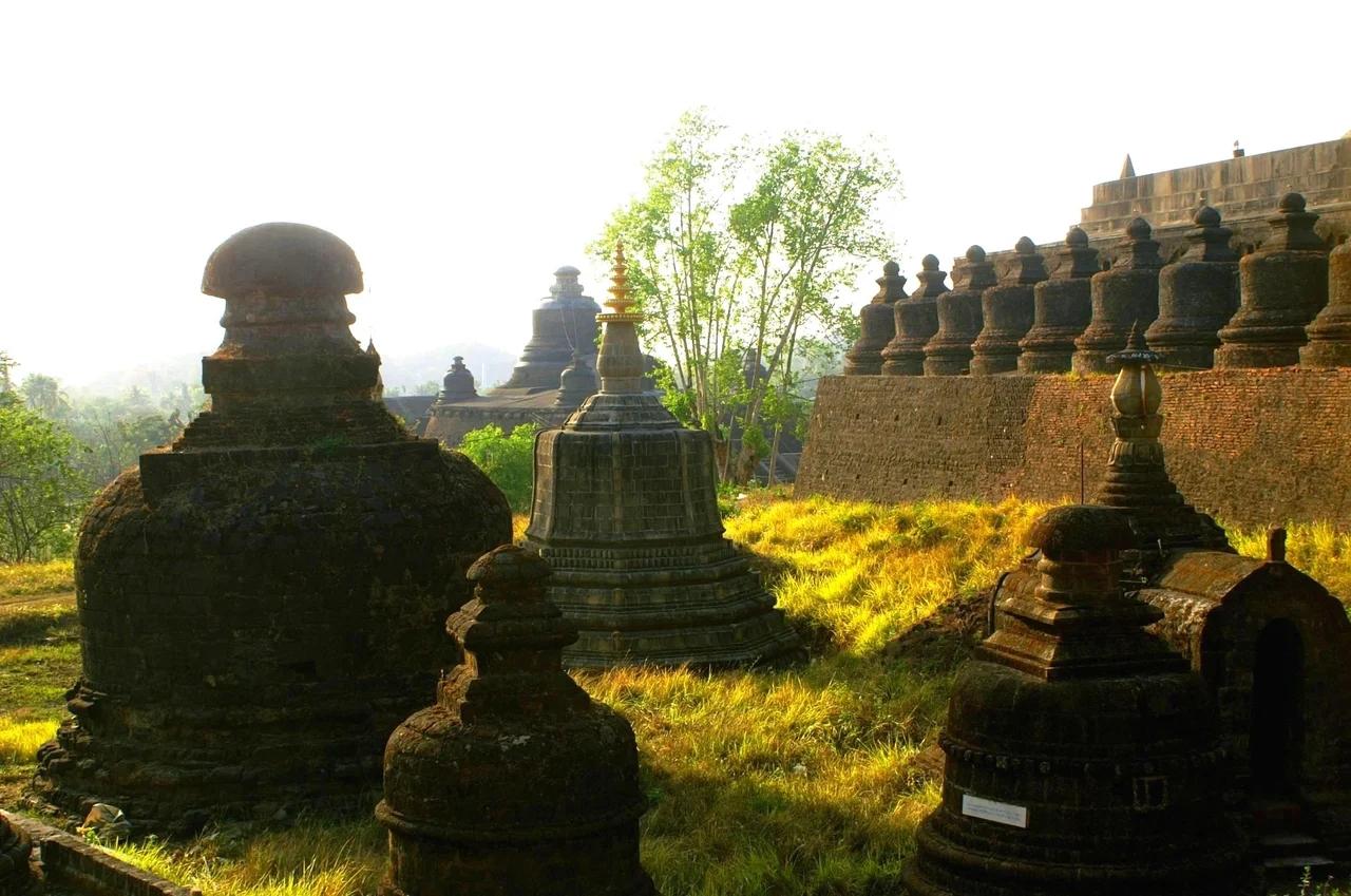The temple was built in 1535 to 1536 by King Min Bin to commemorate his conquest of Bengal. It is located on the western face of Pokhaung Hill, north of the Royal Palace, and adjacent to the Andaw-thein temple. It is typical of the many Buddhist temples found in Burma: a central bell-shaped stupa, surrounded by four smaller stupas at the corners, and a multitude of even-smaller stupas surrounding them.
In back far, the Dukkanthein temple